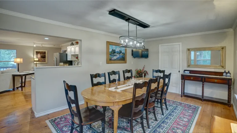 Dining room with long wooden table and chairs on patterned rug.